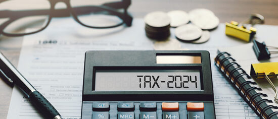 Word Tax 2024 on the calculator. Business and tax concept.Calculator, coins, book, tax form, and pen on table.Tax deduction planning.Financial research, government taxes, and calculation tax return